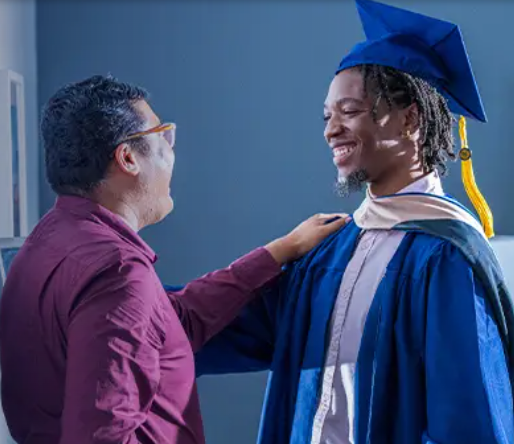 A man is smiling at a graduate with his cap and gown on.